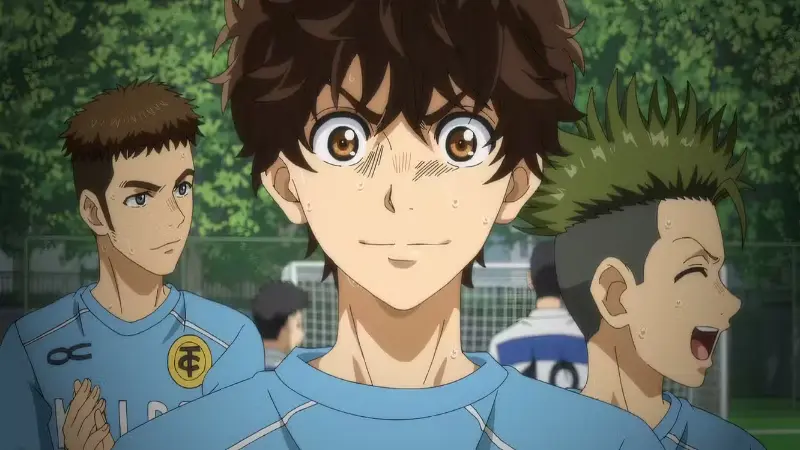 Ashito Aoi smiles with intense determination, his face covered in sweat, while standing on the soccer pitch with his teammates in the background.
