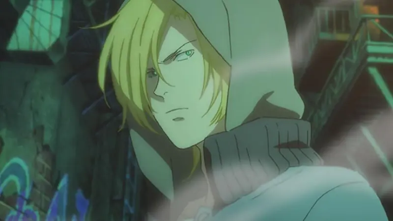 Ash Lynx glances back sharply over his shoulder, wearing a grey hoodie in a dark, misty alleyway in the crime drama Banana Fish.