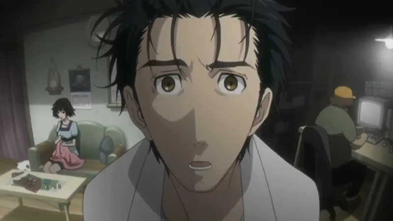 Rintaro Okabe stares forward with a panicked, horrified expression inside his cluttered laboratory in the psychological thriller Steins;Gate.