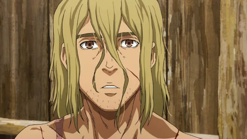 An older, weary Thorfinn looks forward with dull eyes and unkempt blonde hair in front of a wooden wall in the historical drama Vinland Saga.