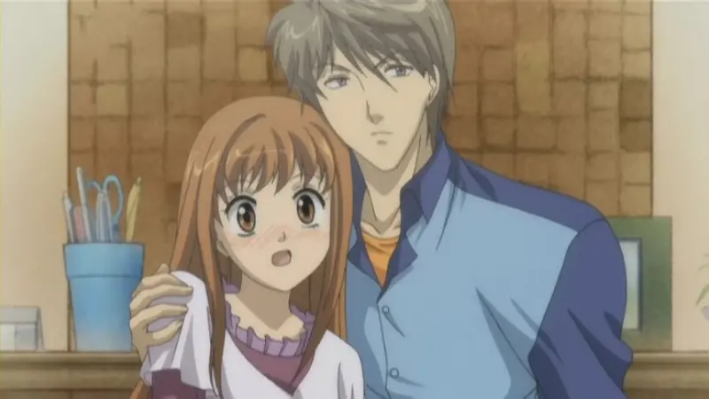 Naoki stands behind a surprised Kotoko with his hands gently resting on her shoulders inside their home.